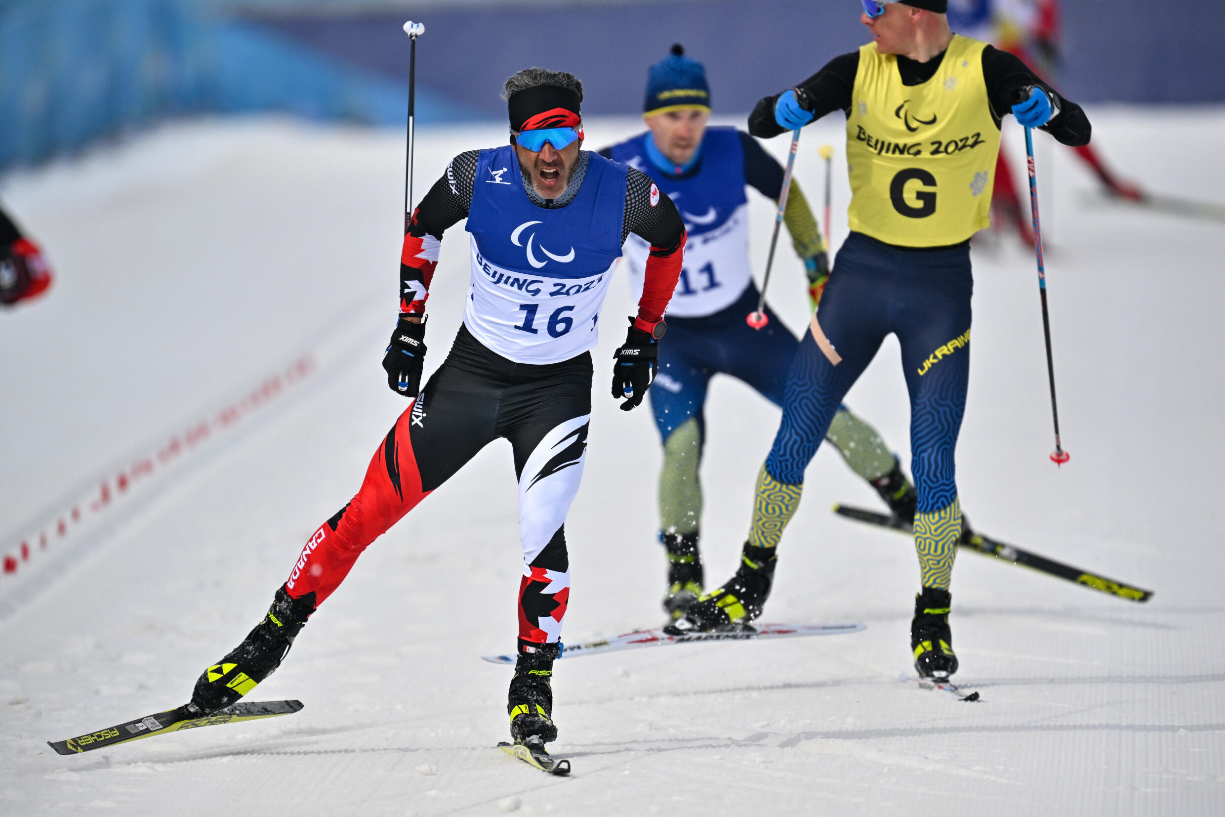 Brian McIver (C) du Canada se dirige vers la ligne d'arrivée lors de la course masculine de mi-distance sans vue et basse vision lors de l'événement de ski de fond du 12 mars.
