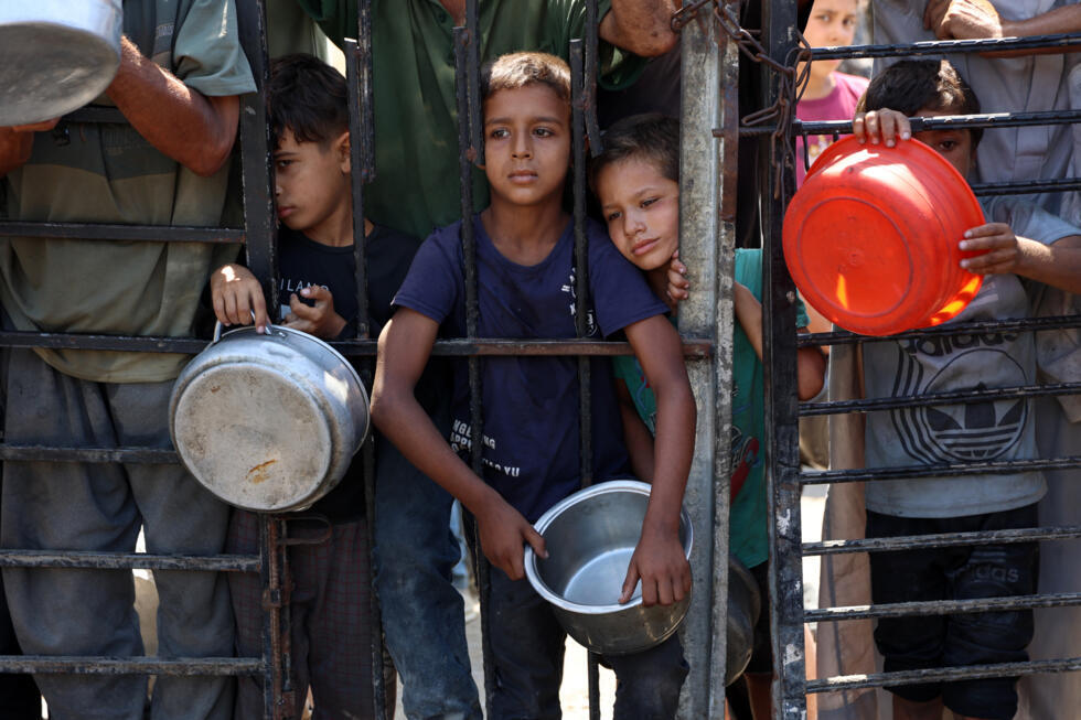 Des enfants palestiniens attendent de recevoir de la nourriture devant une organisation de charité locale distribuant du riz cuit, dans la ville de Gaza, le 23 août 2025