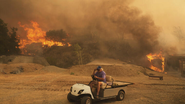A resident rides a golf cart as he exits his property while the Canyon Fire burns on Thursday, Aug. 7, 2025, in Hasley Canyon, California.