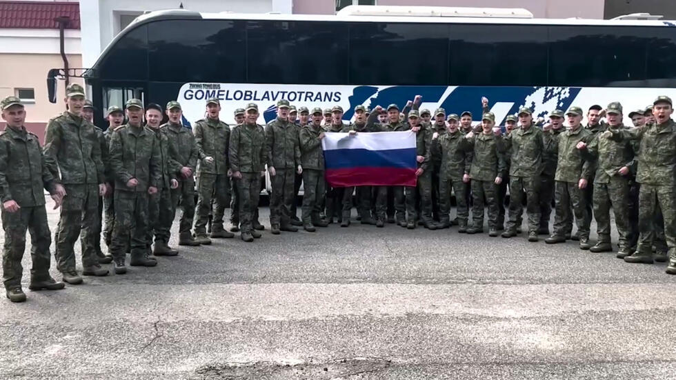 Image tirée d'une vidéo diffusée par le ministère russe de la Défense, le 9 juin 2025, de prisonniers de guerre russes tenant un drapeau russe devant un bus après un échange dans un lieu non divulgué au Bélarus