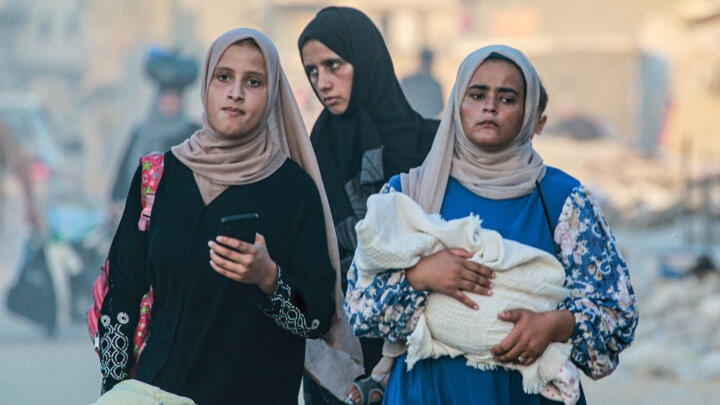 A woman holds a baby wrapped in a blanket as displaced Palestinians leave an area in Khan Younis after the Israeli army issued a new evacuation order.