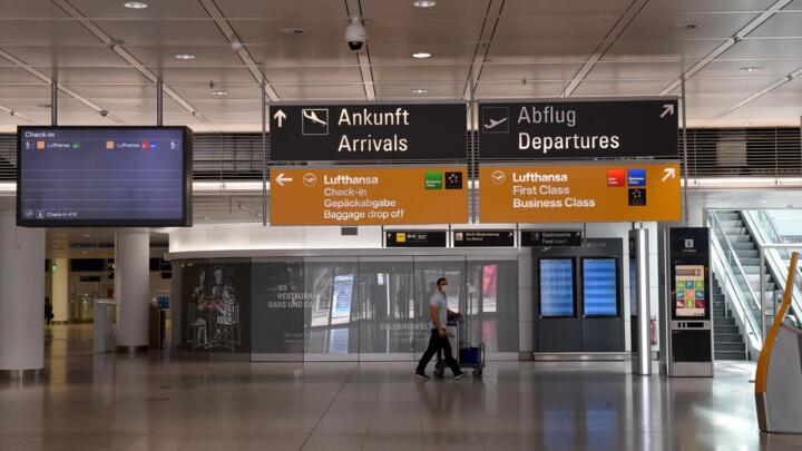 Passengers walk under a board in an empty terminal of the German airline Lufthansa at the "Franz-Josef-Strauss" airport in Munich, southern Germany, on June 3, 2020.