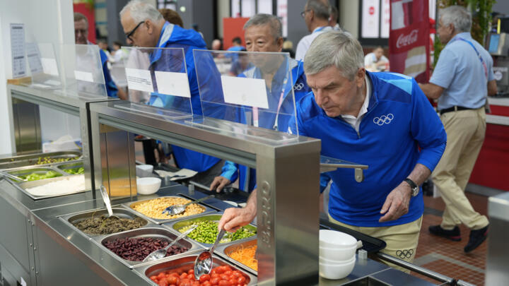IOC President Thomas Bach tries food from a salad bar while touring the Olympic Village ahead of the 2024 Summer Olympics on July 22, 2024.