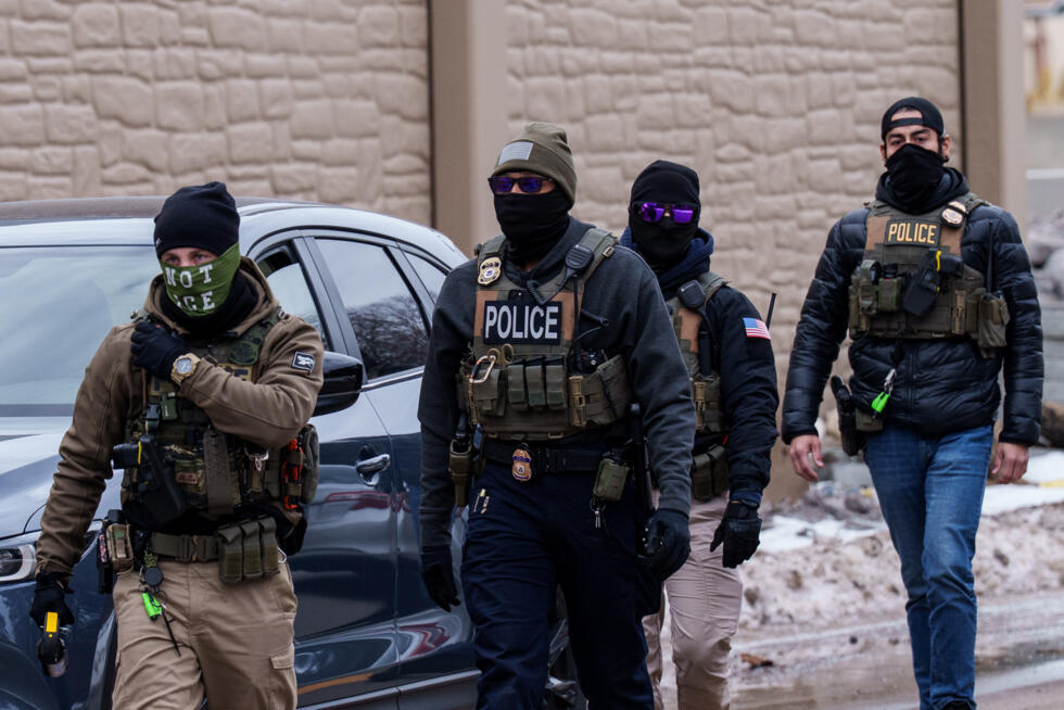 Immigration and Customs Enforcement (ICE) agents, including one wearing a 'NOT ICE' face covering, walk near their vehicles, on January 15, 2026, in Richfield, Minnesota