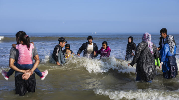 Migrants with children walk in the water as they try to board a smuggler's boat in an attempt to cross the English Channel off the beach of Equihen, northern France, June 30, 2025.