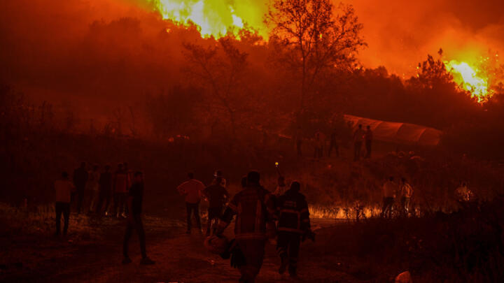 Residents and firefighters attempt to extinguish a wildfire as smoke and flames rise from a forested area in the Gursu district of Bursa early on July 27, 2025.