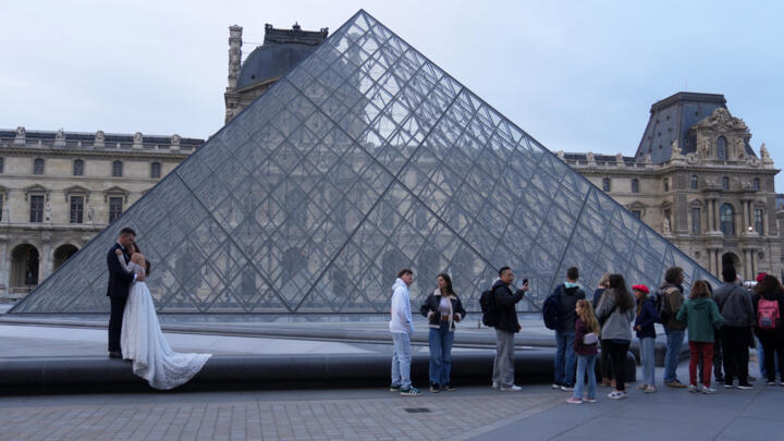 A wedding couple poses for photographs as visitors line up to enter the Louvre on October 22, 2025.