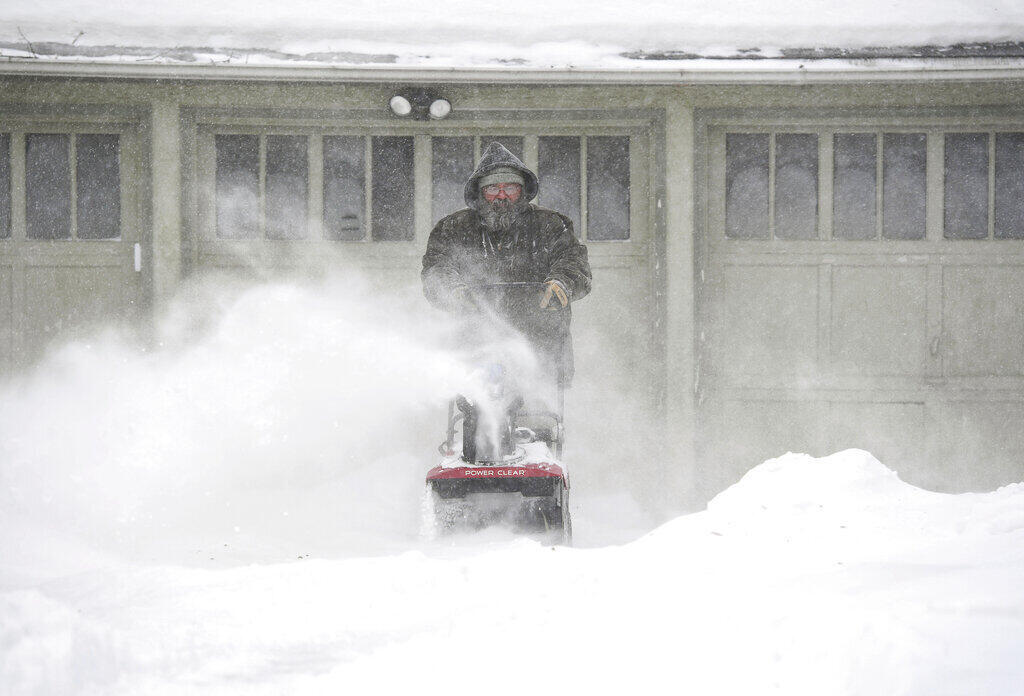 la nieve cae alrededor de David Dailey, mientras este usa un apaarato para apartarla de ujnas puertas. El miércoles 22 de febrero de 2023 en Sioux Falls, Dakota del Sur.