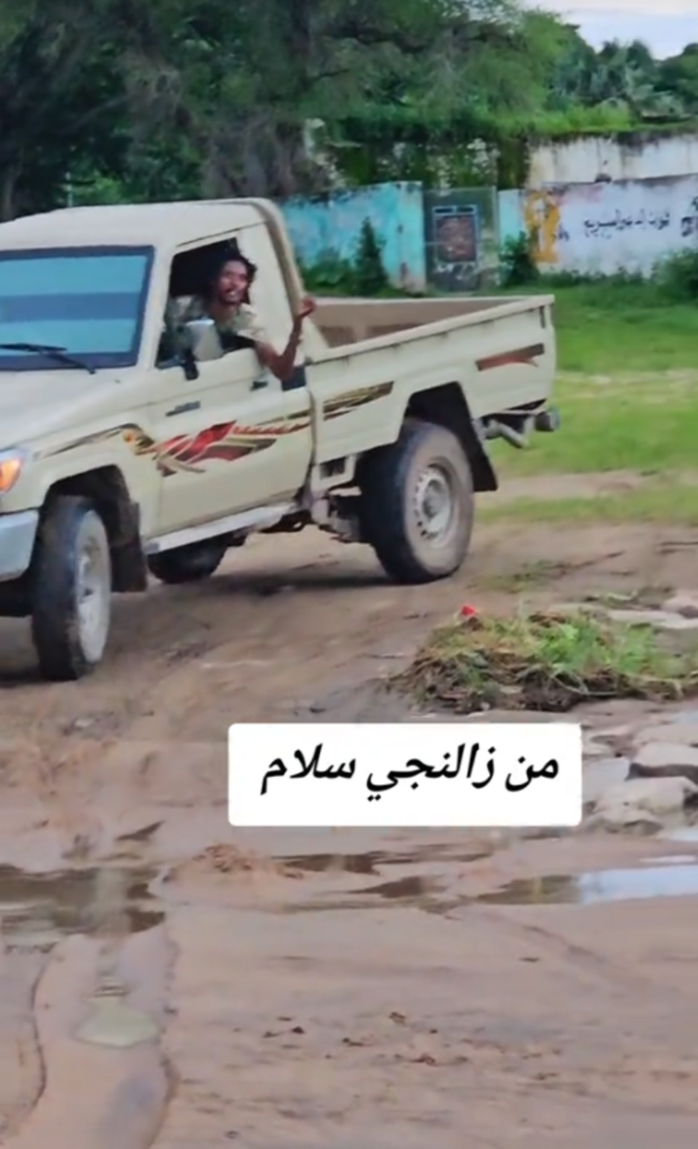 This screenshot shows the man driving his pickup truck in front of a base that has the words "Rapid Support Forces" written on it.