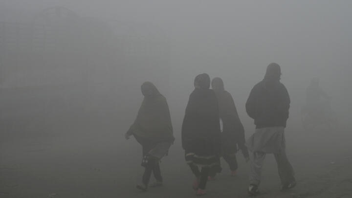 People walk through heavy smog on the outskirts of Lahore on December 14, 2023.