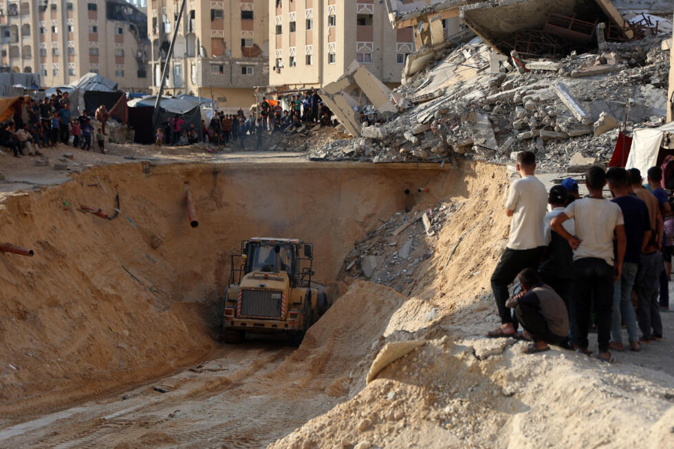 Des Palestiniens regardent une pelleteuse creuser dans le sol à la recherche apparemment de corps à Khan Younès, dans le sud de la bande de Gaza, le 17 octobre 2025
