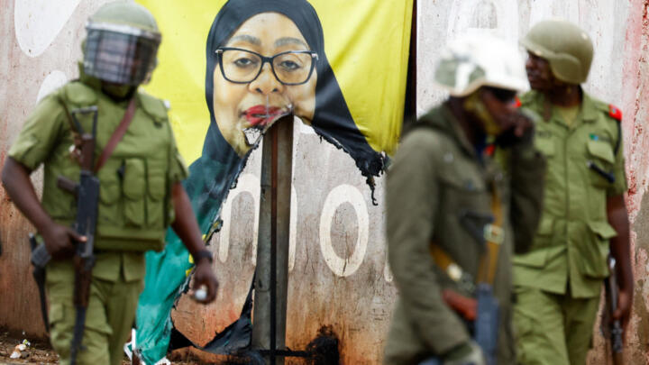 Riot police walk by a vandalised campaign poster of President Samia Suluhu Hassan, following a post-election protest in Tanzania, on October 30, 2025.