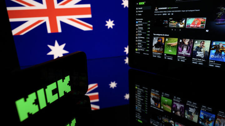 This photograph shows screens displaying the logo and the home page of the Australian live-streaming platform Kick with the Australian flag in the background.