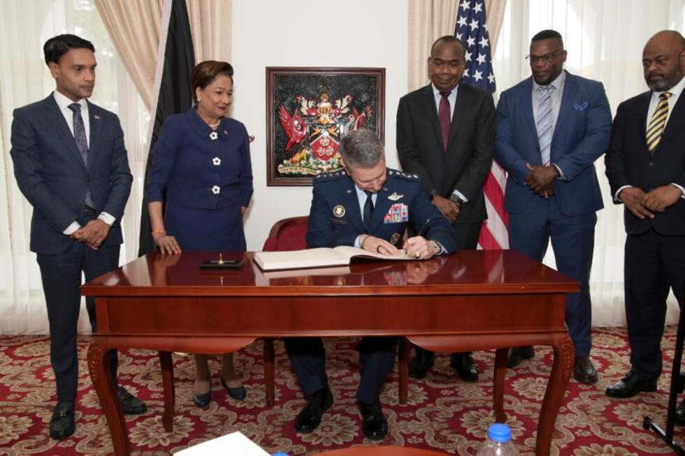 Photo diffusée par le bureau de presse de la présidence de Trinité-et-Tobago montrant le chef d'état-major américain, le général Dan Cain (c)e, signant un document avec la Première ministre de Trinité-et-Tobago, Kamla Persad-Bissessar (2e g), lors de sa visite à Port of Spain, le 25 novembre 2025
