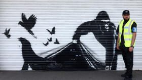 A security guard stands beside an artwork by street artist Banksy, the ninth to released in nine days, depicting a gorilla releasing animals, on the front of a shutter outside London zoo, on August 13, 2024.