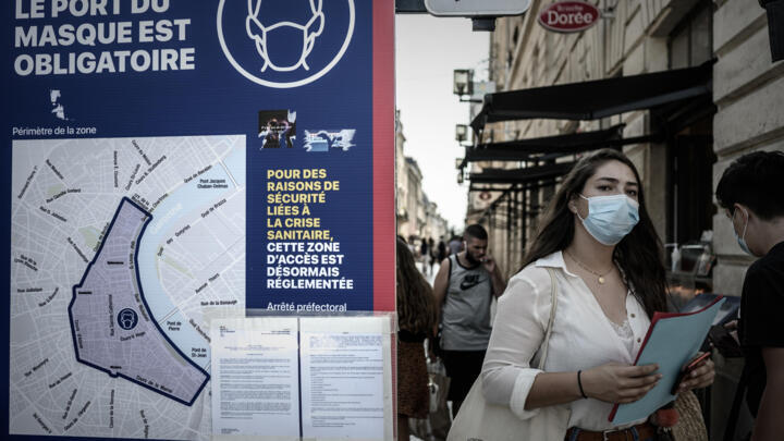 A woman wearing a face mask walks past a sign showing the area where wearing a mask is mandatory due to Covid-19 health measures in Bordeaux, southwestern France, on September 16, 2020.