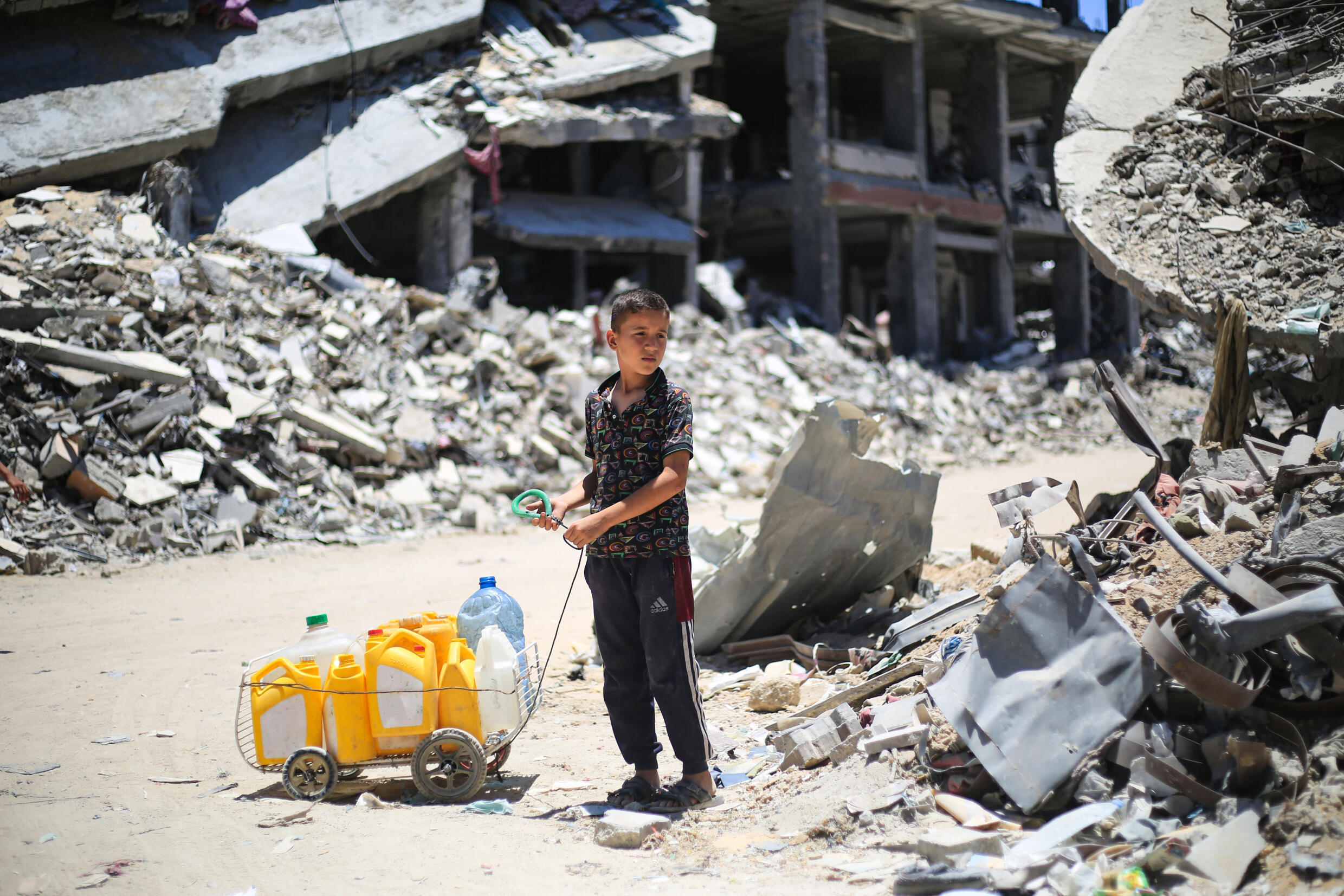 Un garçon palestinien transporte des bidons d'eau au milieu des destructions à Khan Younés, dans le sud de la bande de Gaza, le 3 juillet 2024