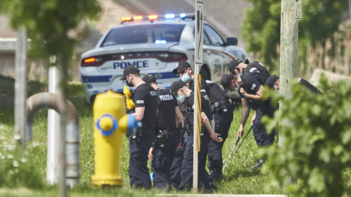 A line of police officers look for evidence at the scene of a car crash in London, Ontario on Monday, June 7, 2021. Police say multiple people have died after several pedestrians were struck by a car Sunday night.
