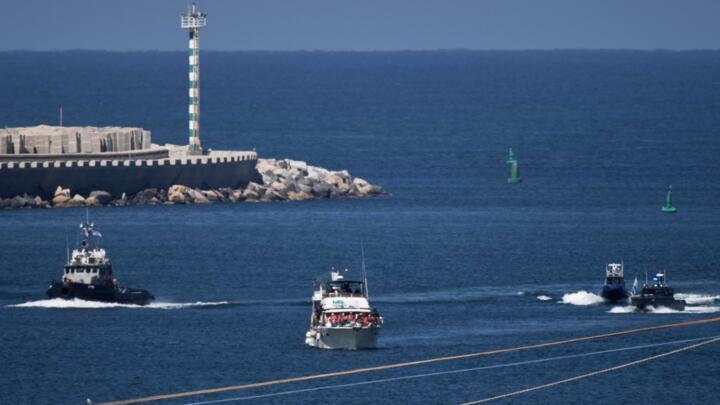 Activists in orange life jackets sit aboard a Gaza-bound Sumud flotilla boat as Israeli navy soldiers sail it into the port of Ashdod, Israel.