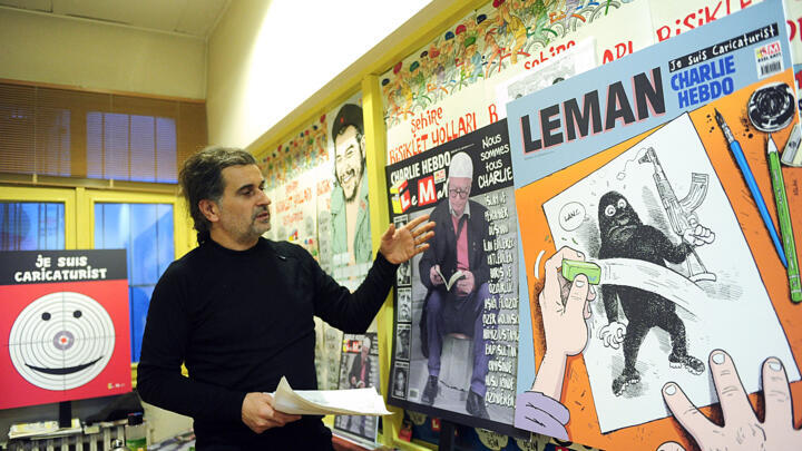 The director of the satirical Turkish magazine Leman, Zafer Aknar, stands in his office next to a poster of the French satirical weekly Charlie Hebbo (L) on January 12, 2015 in Istanbul.