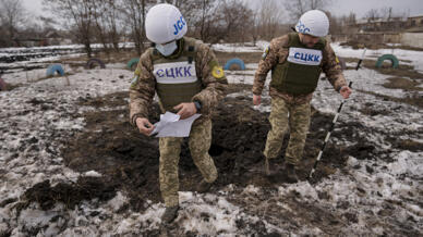 Los miembros del Centro Conjunto para el Control y la Coordinación del cese al fuego de la línea de demarcación examinan un cráter de un proyectil de artillería que cayó cerca de una escuela en Vrubivka. Lugansk, Ucrania, 17 de febrero, 2022.