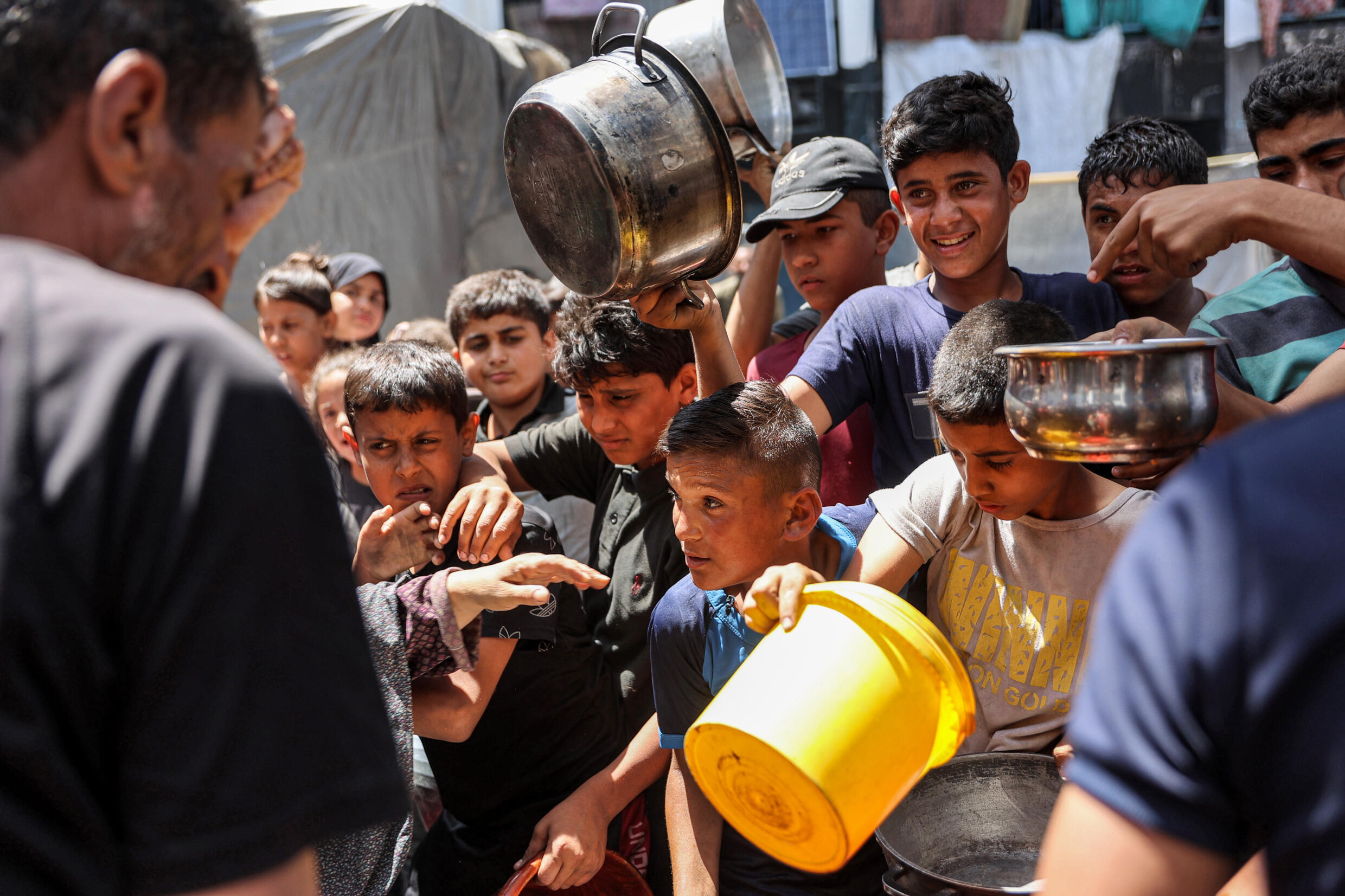 Des enfants font la queue avec des récipients pour recevoir de la nourriture dans une cuisine gérée par l'agence de l'ONU pour les réfugiés palestiniens (Unrwa), dans le camp de Jabalia dans le nord de la bande de Gaza, le 13 juin 2024