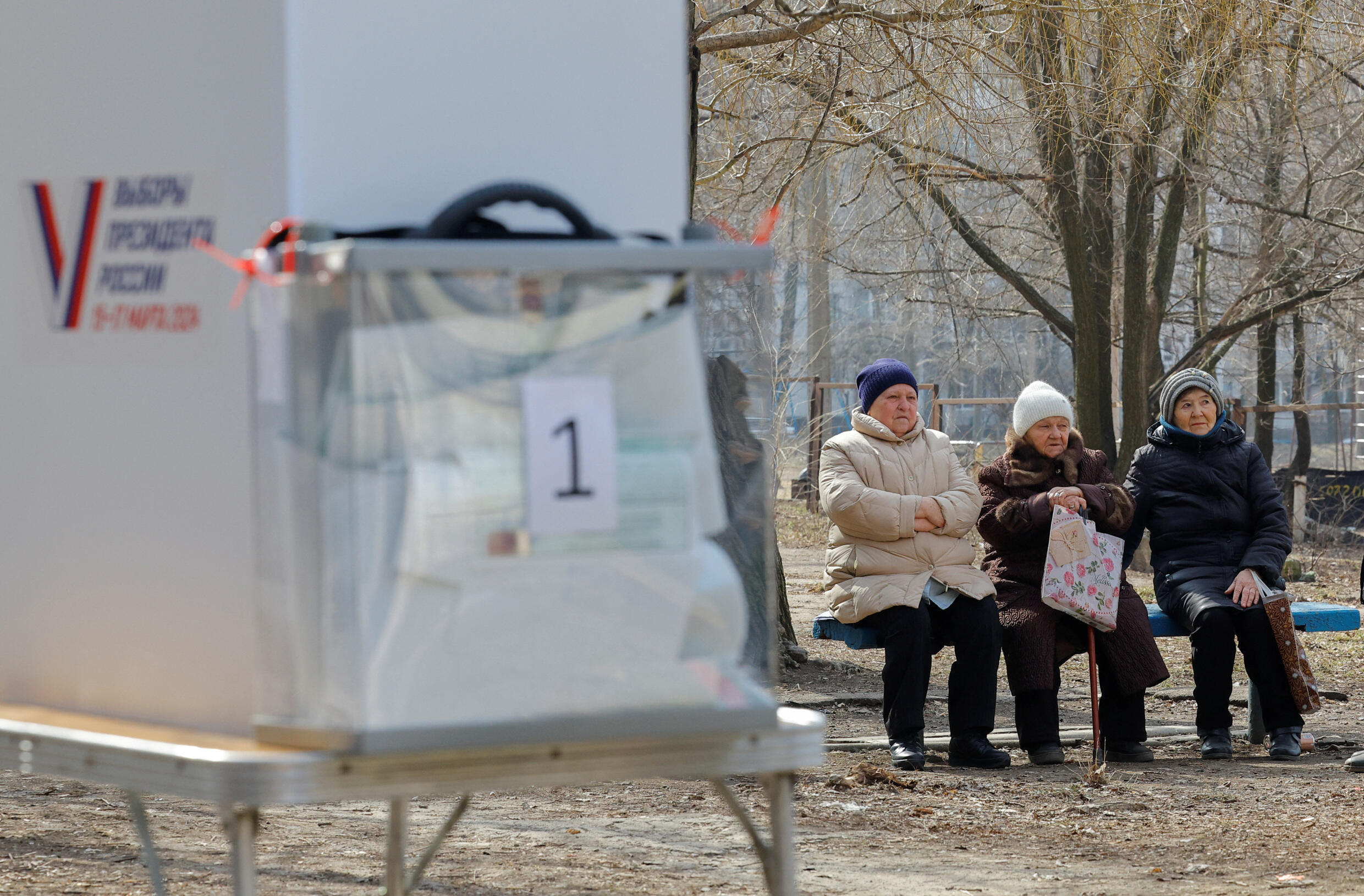 Three women sit on a bench near a mobile polling station during the early voting in Russia’s presidential election, in Donetsk, Russian-controlled Ukraine, on March 10, 2024.