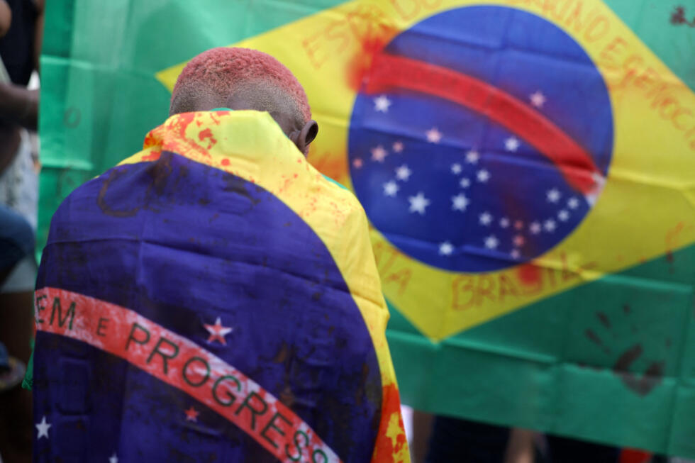 A person draped in a Brazilian flag marked with fake blood stains attends a protest in Rio de Janeiro a day after a deadly police operation against drug trafficking at the favela do Penha, on October