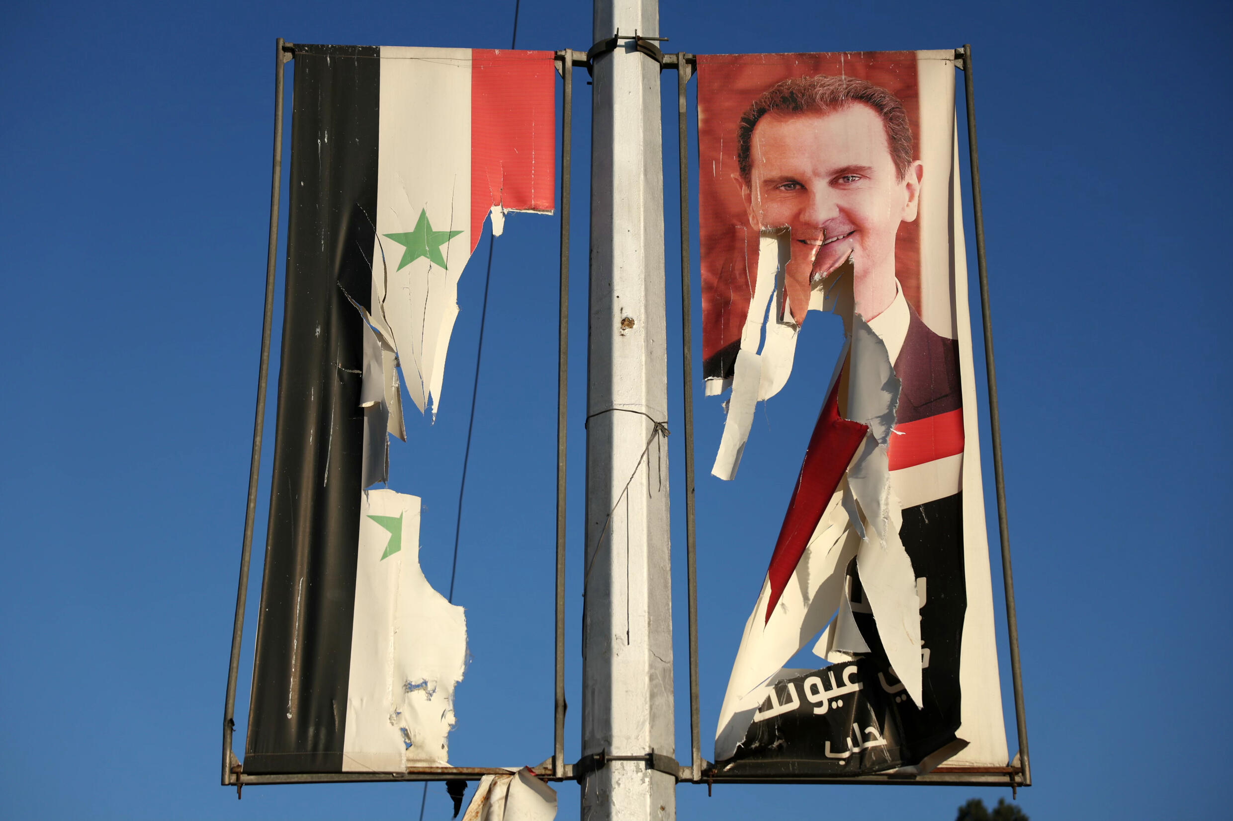 Un drapeau national syrien et un portrait du président syrien Bachar al-Assad dséchirés par des combattants antigouvernementaux dans la ville d'Alep, dans le nord de la Syrie, le 30 novembre 2024.