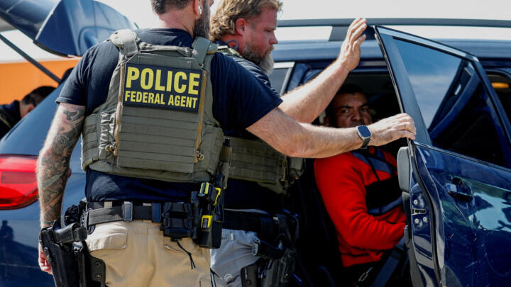 ICE agents detaining migrants in parking lot.