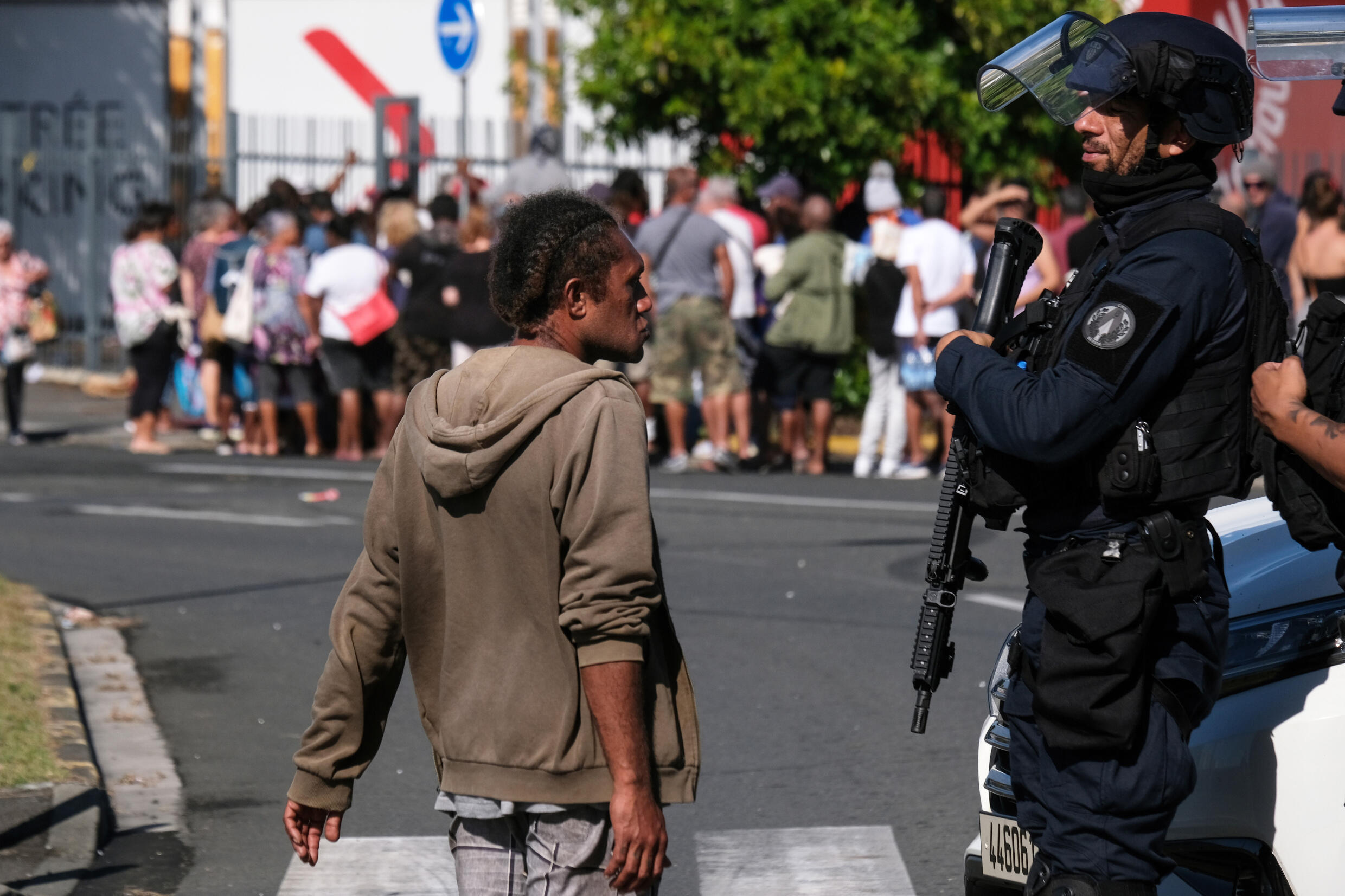 Un policier parle avec un habitant à Noumea en Nouvelle-Calédonie devant une file d'attente pour entrer dans un supermarché le 18 mai 2024