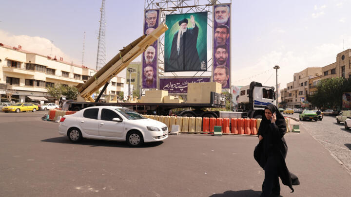 A woman walks past a deactivated missile and a giant portrait of Iranian Supreme Leader Ayatollah Ali Khamenei in Tehran on September 27, 2025.