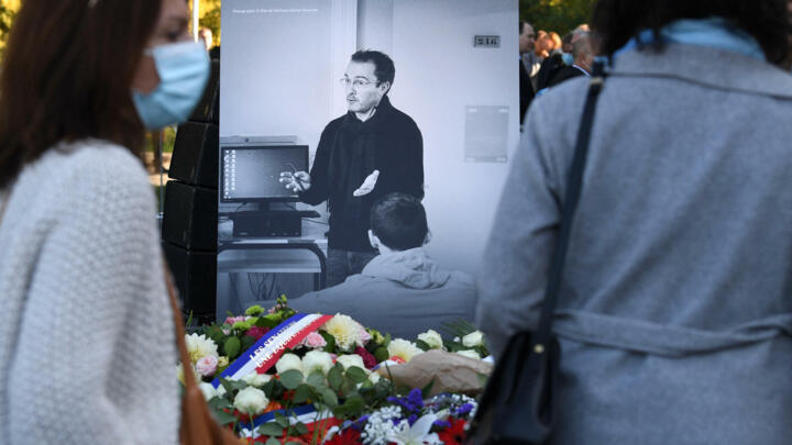 People stand in front of a photograph showing French history and geography teacher Samuel Paty at a tribute ceremony held one year after Paty’s death in Eragny-sur-Oise, northwestern Paris, on October 16, 2021.