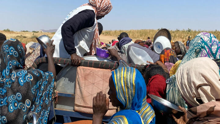 Sudanese civilians who fled Darfur's El-Fasher city after it was overrun by paramilitary forces receive food at a camp in Tawila on November 2, 2025.