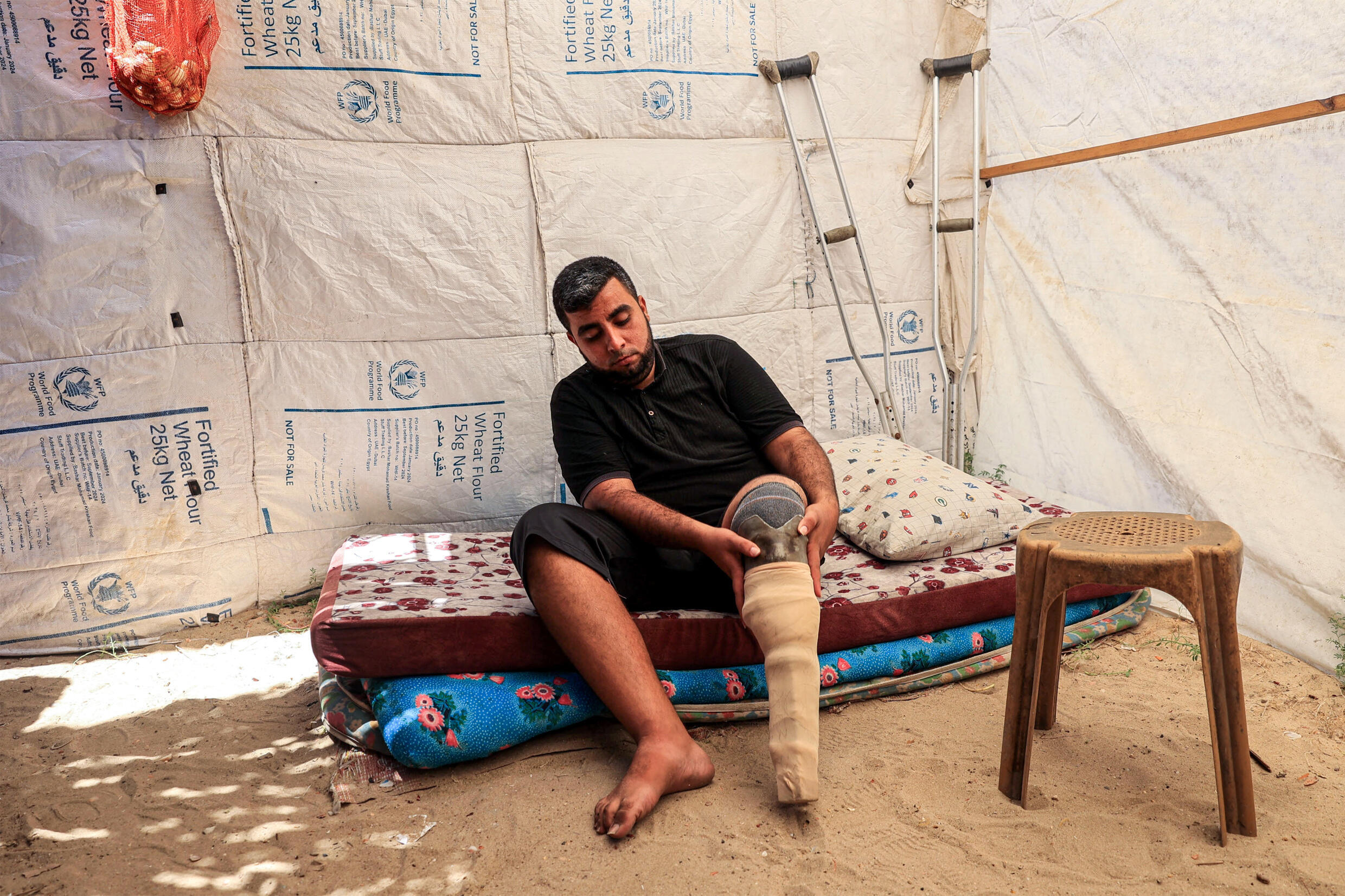 Majed-al-Imari, un déplacé palestinien de 32 ans amputé après des blessures durant le conflit en cours à Gaza fixe une prothèse dans une tente à Deir-al-Balah, le 6 juillet 2024.
