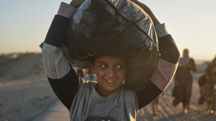 A displaced Palestinian girl carries a bag on her head as she walks along the coastal road near Wadi Gaza in the central Gaza Strip on October 10, 2025.