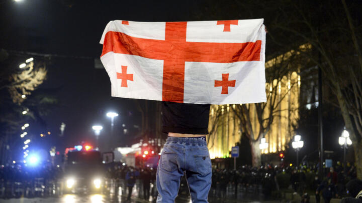 Un manifestant contre le projet de loi sur les "agents de l'étranger" tient un drapeau de la Géorgie devant une ligne de police à l'extérieur du bâtiment du Parlement à Tbilissi, le 9 mars 2023.