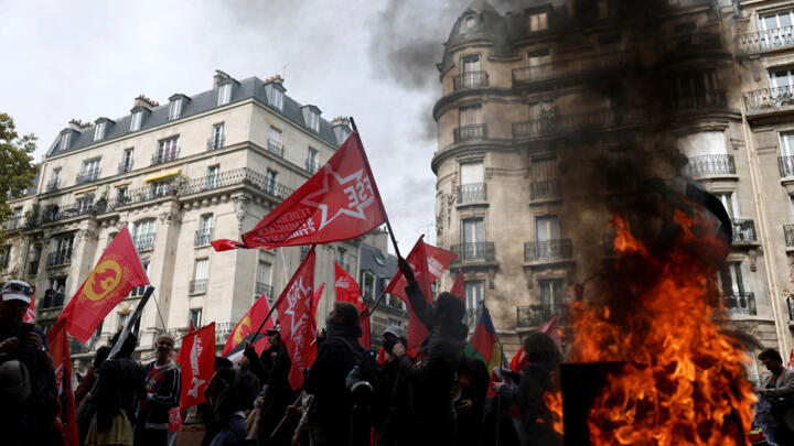 Protesters holding flags walk past a burning garbage bin during a demonstration in Paris, France, October 2, 2025.