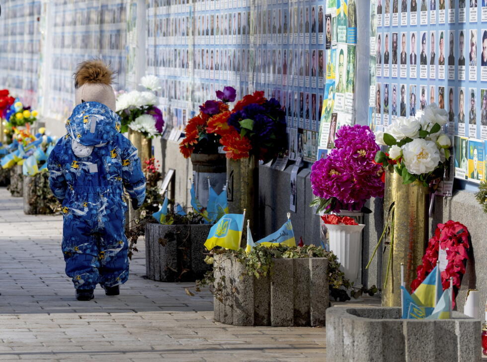 Un niño pasa junto al muro de la memoria con fotos de miles de ucranianos muertos desde el comienzo de la guerra con Rusia en Kiev, Ucrania, el domingo 23 de febrero de 2025.