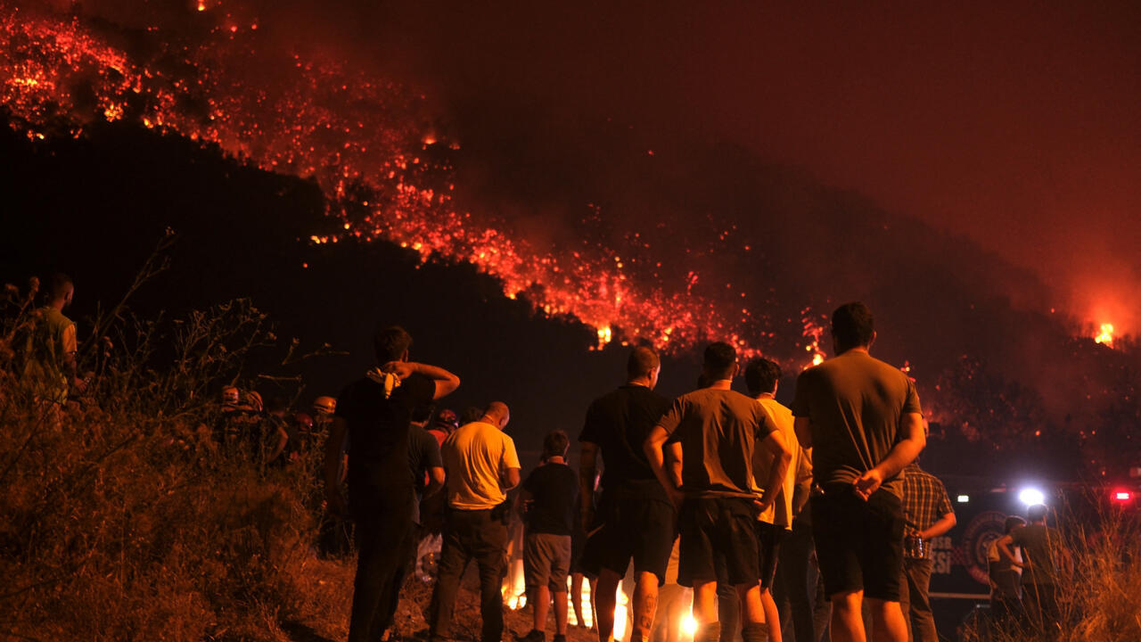 Residents and firefighters attempt to extinguish a wildfire as smoke and flames rise from a forested area in Bursa, Turkey early on July 27, 2025.