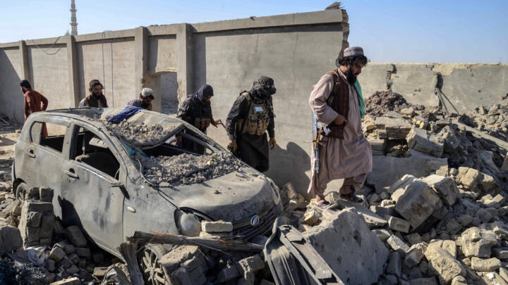 Taliban security personnel walk past a damaged car in the Spin Boldak district of Kandahar province on October 16, 2025.