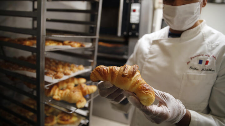A French baker holds up a croissant in his bakery on March 26, 2020.
