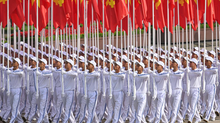 Men carry Vietnamese national and party flags during a parade marking Vietnam's 80th National Day celebrations in Hanoi on September 2, 2025.