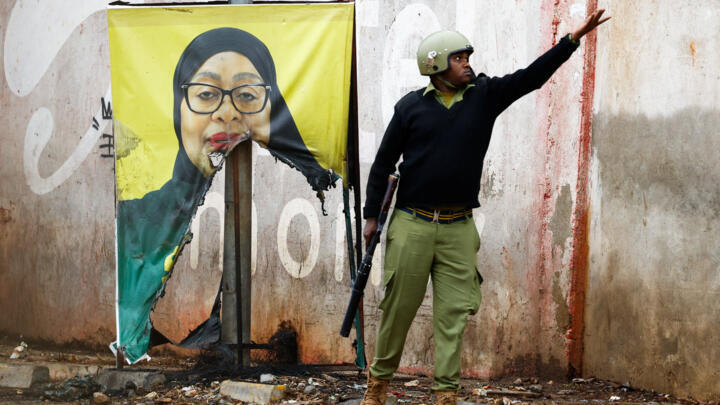 A riot police officer throws a used teargas canister near a vandalised campaign poster of President Samia Suluhu Hassan at the Namanga One-Post Border crossing point in Tanzania on October 30, 2025.