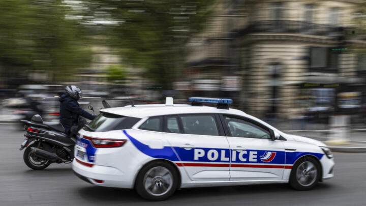 A French police officer drives a police car next to a scooter on a street in Paris.