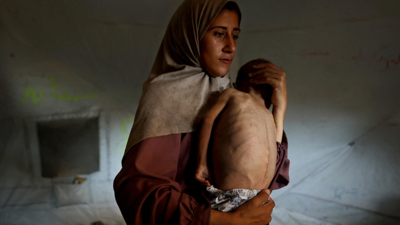 Une Palestinienne porte son fils de 18 mois, qui présente des signes de malnutrition, dans le camp de réfugiés d'Al-Shati, à l'ouest de Gaza, le 24 juillet 2025.