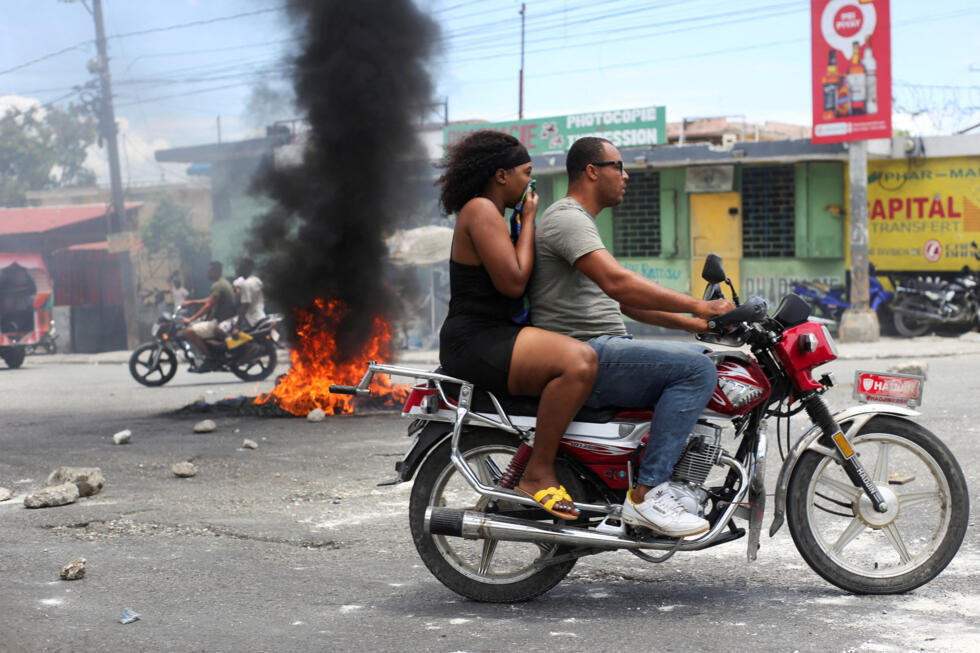 Un motociclista pasa junto a una barricada en llamas durante una protesta contra la violencia relacionada con las bandas y para exigir la dimisión del consejo presidencial de transición de Haití, en Puerto Príncipe, Haití, 15 de mayo de 2025.