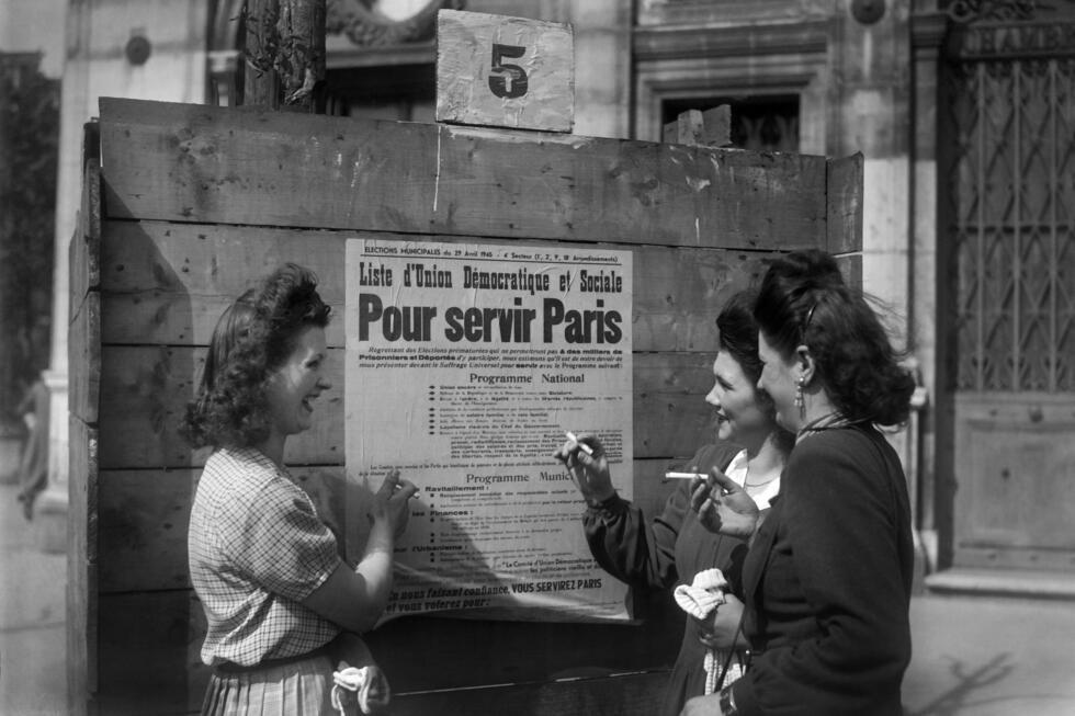 Des femmes devant une affiche électorale pour les élections municipales, avant de voter pour la première fois en France, le 29 avril 1945 à Paris.