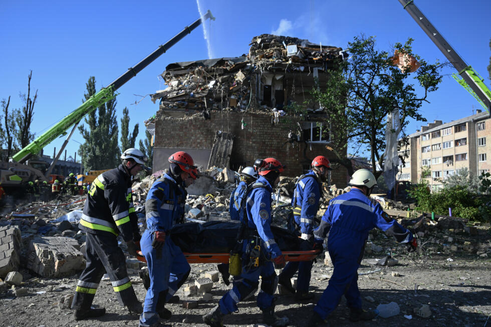 Des sauveteurs ukrainiens transportent le corps d'une victime près d'un immeuble résidentiel fortement endomagé lors d'une attaque massive de drones et de missiles russes sur Kiev, le 28 août 2025.
