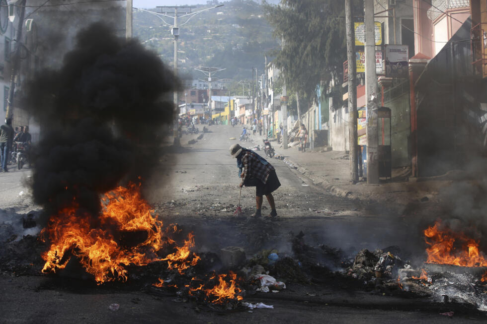 Una mujer barre los escombros junto a una barricada en llamas levantada por manifestantes durante una protesta contra la inseguridad en Puerto Príncipe, Haití, el 2 de abril de 2025.